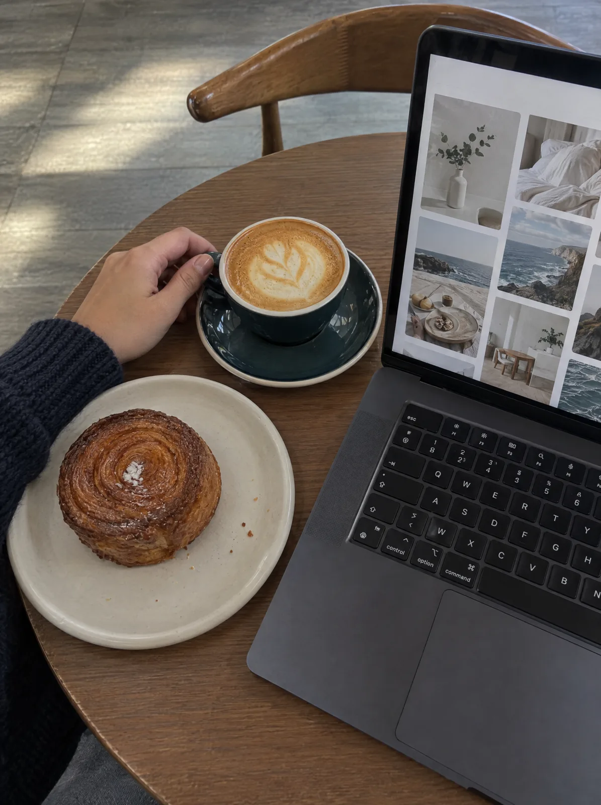 Ein Laptop, Kaffee und Gebäck stehen auf einem Cafétisch.